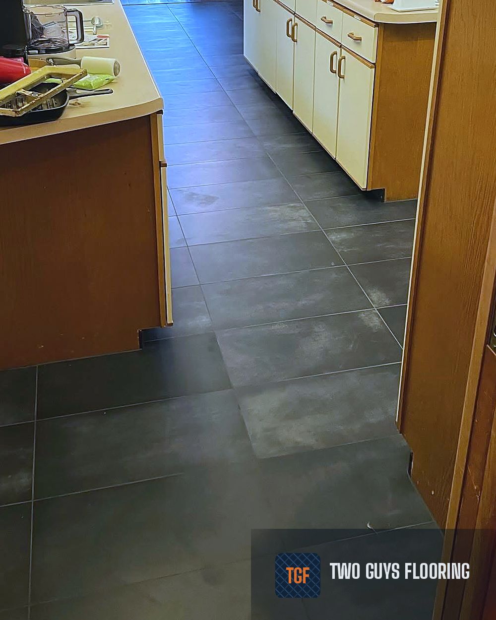 The same kitchen after — large-format charcoal porcelain tile replacing the carpet