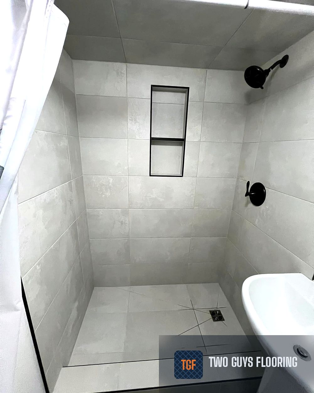 The same bathroom after — a fully tiled walk-in shower with black fixtures and a built-in niche