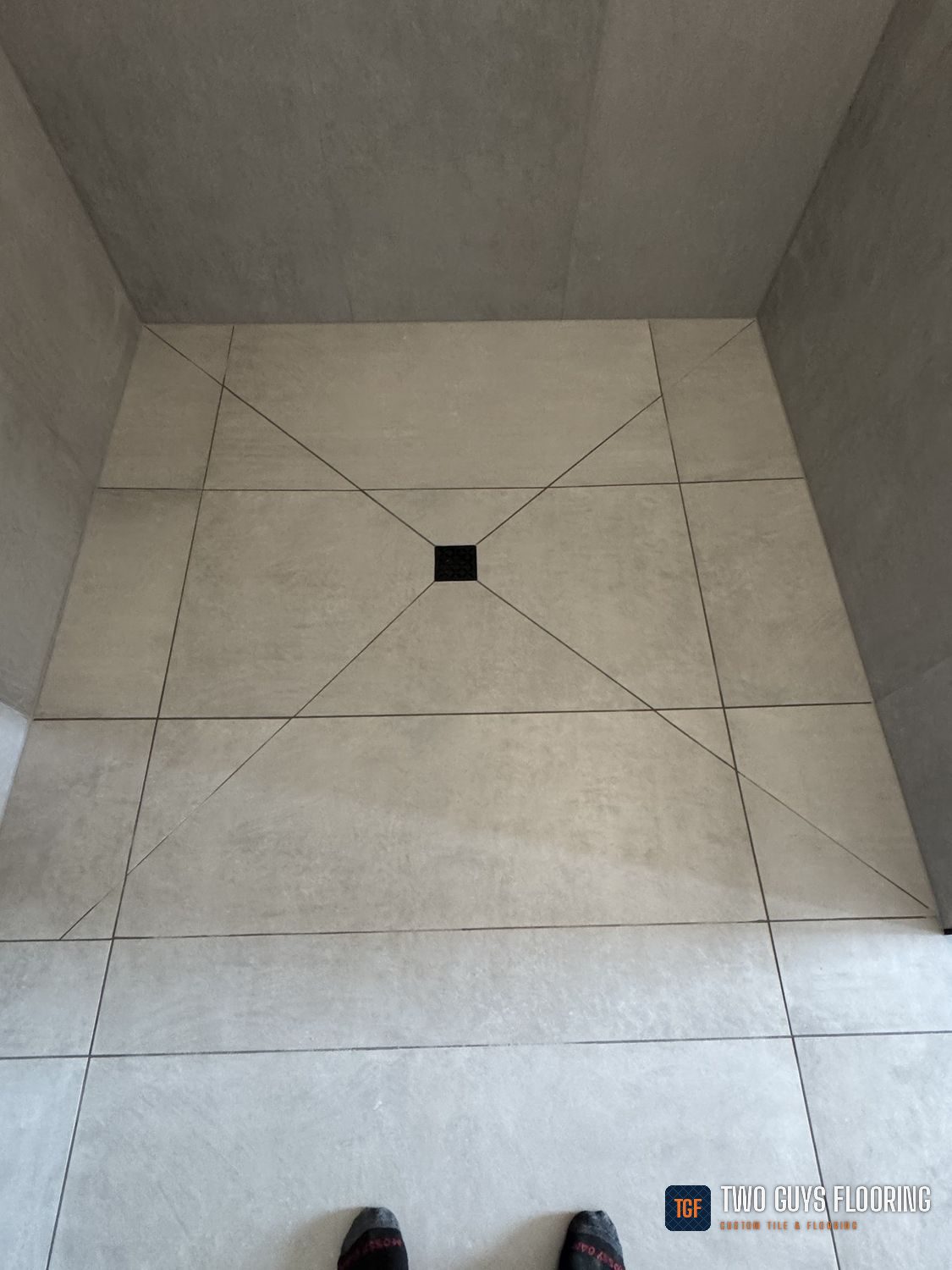 A curbless shower floor in large-format tile, cut to a four-way pitch to the center drain